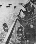 COAST GUARD-MANNED LANDING BARGES ARE LOWERED AWAY AS DAWN BREAKS OVER GUADALCANAL